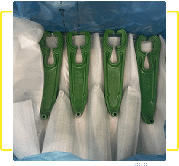 Four green metal levers with cutouts laid out on white cloth.